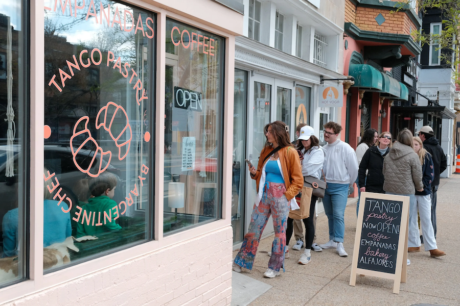 People walking past shops with a large taco mural and a sidewalk menu board